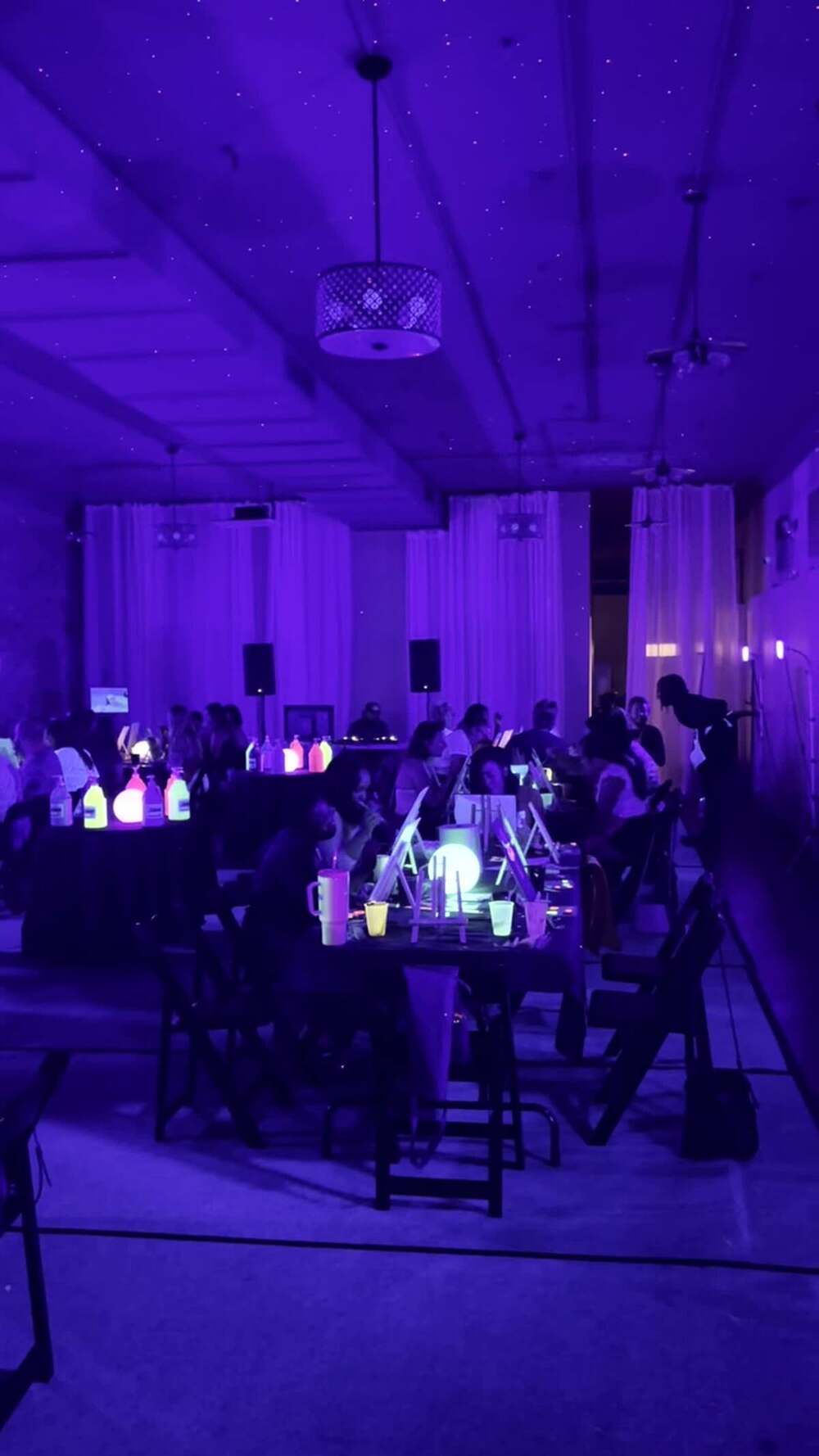 A room of people painting canvases under ultraviolet blacklight